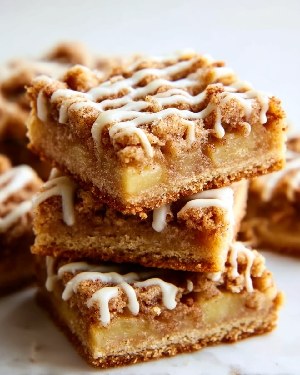 The image shows a close-up of a stack of crumbly apple crumble bars. Each bar has three layers: a golden-brown crumbly crust at the bottom, a soft, light yellow apple filling in the middle that looks juicy and tender, and a crunchy, darker brown streusel topping with small crumbs on top. White icing is drizzled in thin lines over the top of the bars, adding a glossy texture. The bars are stacked unevenly on a white marbled surface, with soft natural light highlighting the textures and colors. photo taken with an iphone --ar 4:5 --v 7