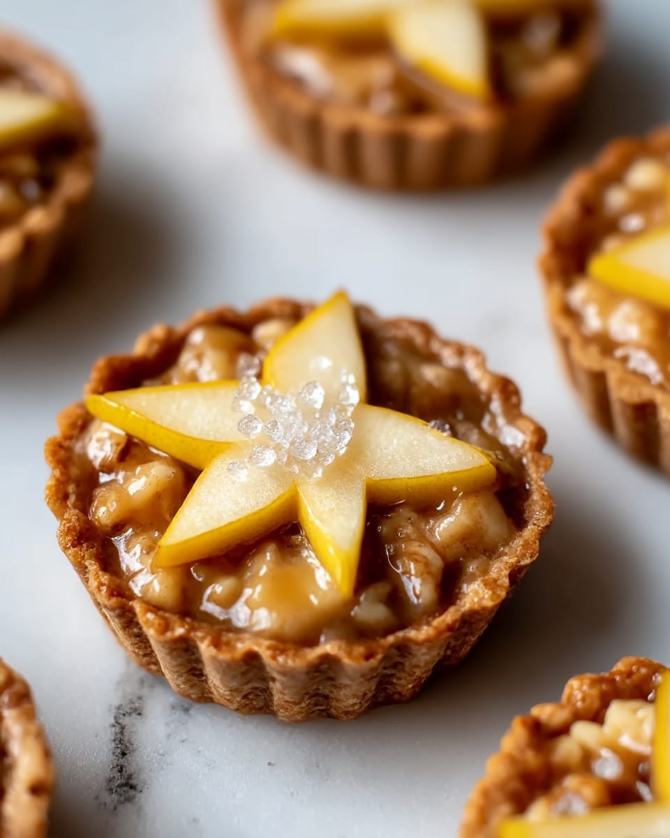 A close-up view of a small tart with a golden-brown crust and chunky walnut pieces baked into it, topped with five pale yellow pear slices arranged in a circular pattern with a cluster of coarse sugar crystals sprinkled in the center. The tart sits on a white marbled surface, showing the shiny, slightly glossy texture of the filling that holds the nuts and fruit together. Other similar tarts are blurred in the background. photo taken with an iphone --ar 4:5 --v 7