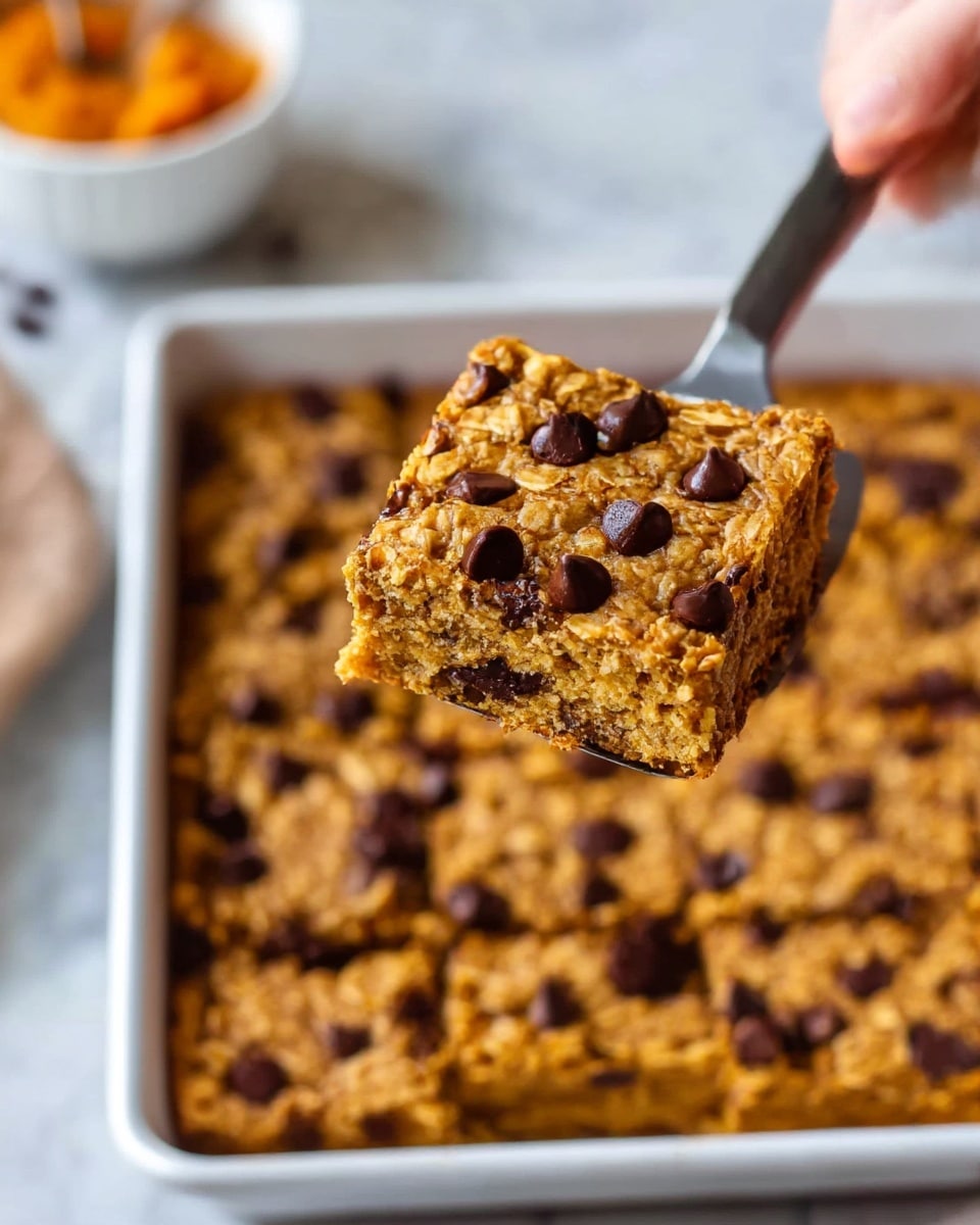 A close-up view of a baked oatmeal bar with chocolate chips, cut into square pieces inside a white baking dish. The bar being lifted shows one thick layer with a rough, crumbly texture in golden brown, dotted with melted dark chocolate chips on top. The inside of the bar is soft with visible oats. In the background, a woman's hand holds the spatula lifting the piece. The scene is set on a white marbled surface. photo taken with an iphone --ar 4:5 --v 7