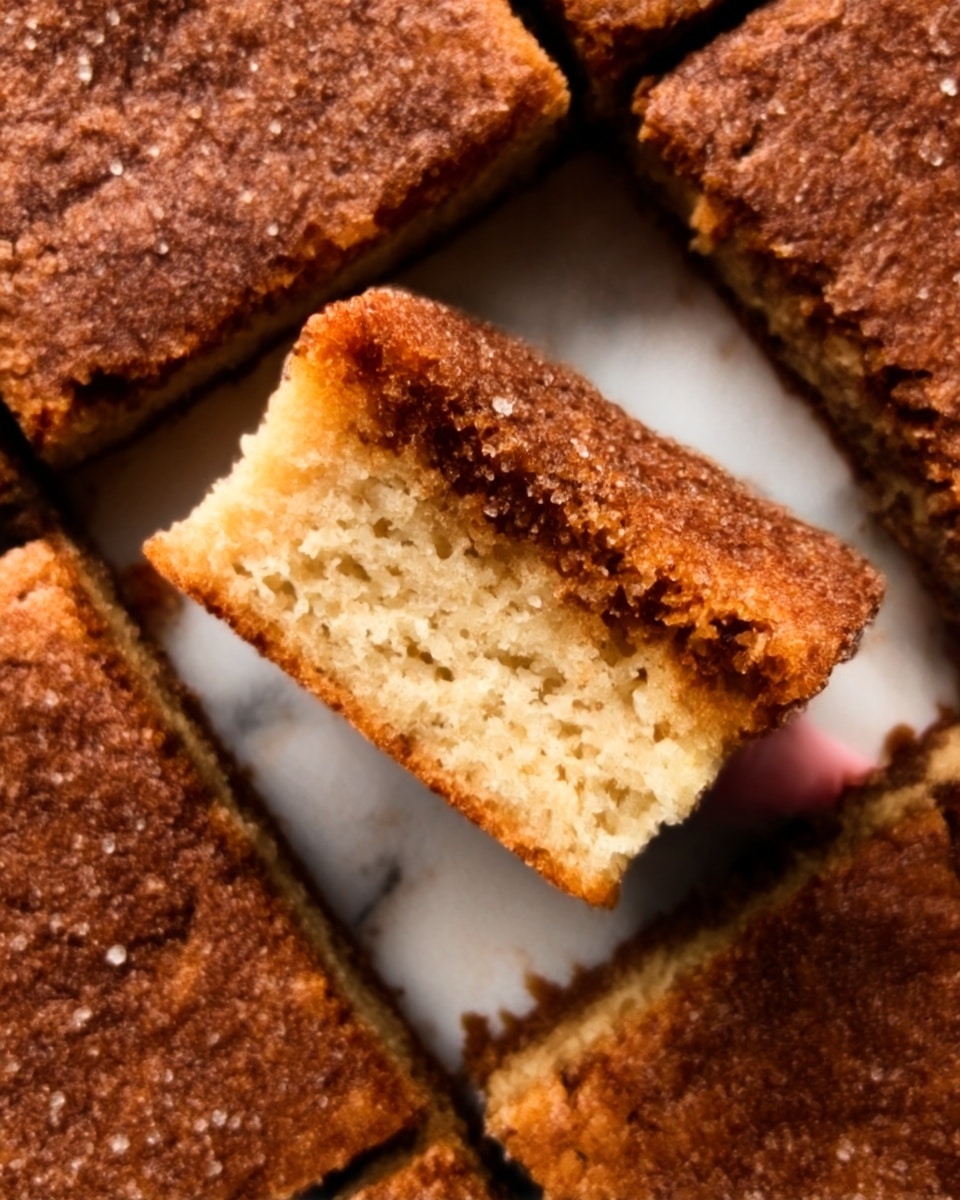 The image shows a close-up of a dessert made of nine square pieces arranged in a 3x3 grid on a white marbled surface. The top crust is dark brown with a crumbly texture and sprinkled with sugar. One square piece in the center is lifted, showing a golden-brown layer beneath the darker top crust, which looks soft and spongy. The edges of the squares are cleanly cut with some crumbs scattered around. Photo taken with an iphone --ar 4:5 --v 7