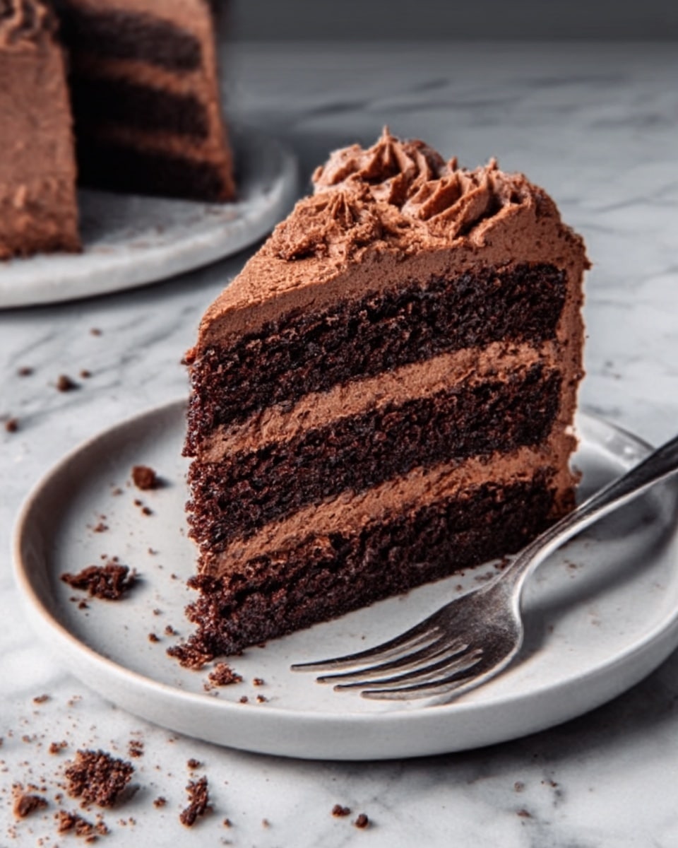 A slice of chocolate layer cake with four visible layers sits on a white plate with a silver fork beside it. Each cake layer is dark brown and moist, separated by smooth, creamy chocolate frosting that is lighter brown. The top of the cake has thick, swirled chocolate frosting with a soft, creamy texture that looks rich and smooth. There are small chocolate crumbs scattered on the white plate and on the white marbled surface around it. The whole scene is bright and clear. Photo taken with an iphone --ar 4:5 --v 7