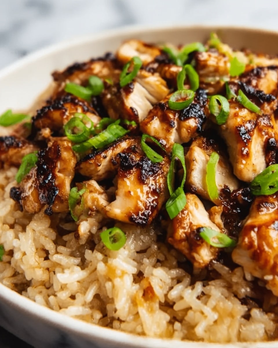 A close-up image of a white plate filled with a bed of light brown cooked rice topped with multiple pieces of glazed grilled chicken. The chicken pieces are golden brown with visible char marks and a shiny, rich brown sauce drizzled over them. Small green scallion slices are scattered on top of the chicken. The whole dish is set against a white marbled surface. Photo taken with an iphone --ar 4:5 --v 7
