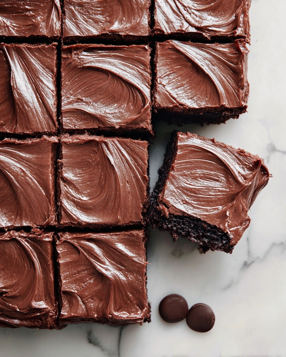 A square chocolate brownie cut into nine equal pieces is shown from above on a white marbled surface. Each brownie piece has a thick top layer of smooth, creamy chocolate frosting with visible swirls and ridges in a rich brown color. The brownie base beneath is darker and slightly textured, showing the dense, moist cake. One brownie piece is pulled out slightly, highlighting its thickness and fudgy texture. Three round chocolate pieces lie next to the brownie on the white marbled surface. photo taken with an iphone --ar 4:5 --v 7