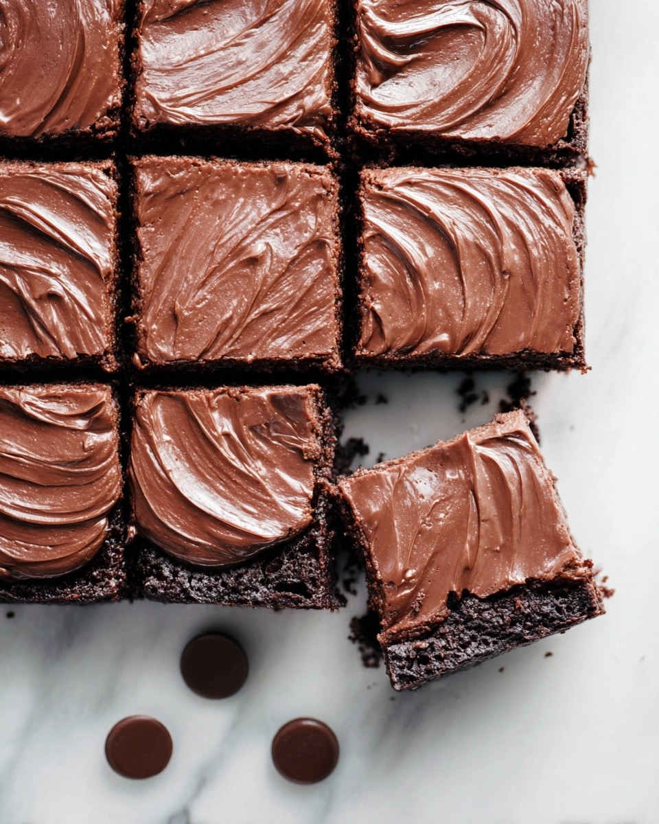 The image shows a close-up of a square chocolate brownie cut into 16 smaller squares, with one piece slightly pulled out from the bottom left corner. Each brownie square has a thick layer of glossy chocolate frosting on top, swirled smoothly with visible texture and shine. The brownie layers underneath appear dense and rich with a dark chocolate color. The dessert is placed on a white marbled surface, and three small round chocolate pieces lie near the bottom edge, adding to the chocolate theme. photo taken with an iphone --ar 4:5 --v 7