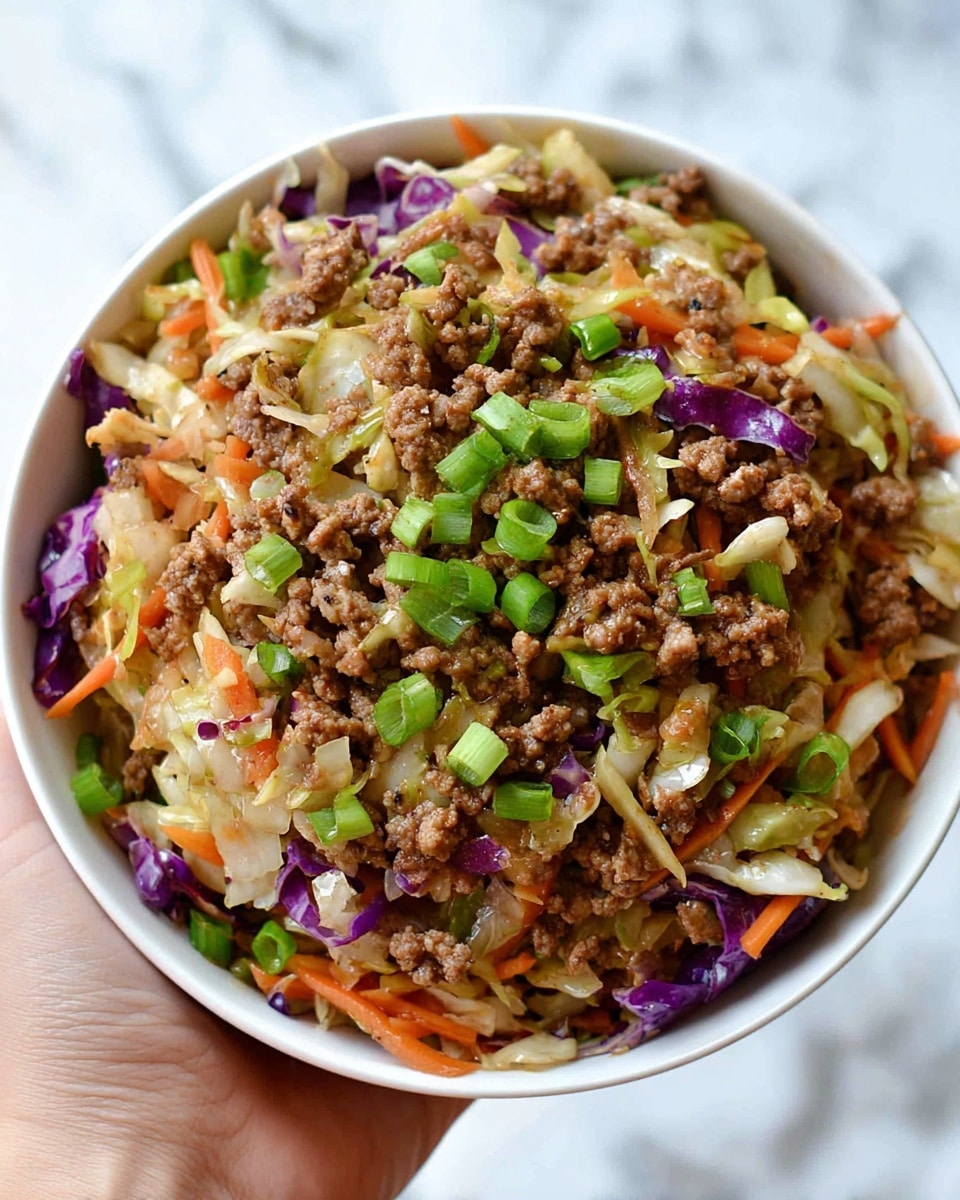 A white bowl filled with a colorful stir fry featuring roughly three main layers: the bottom layer is a mix of shredded white and purple cabbage, thin orange carrot strips, and bits of green onions scattered throughout. The middle layer shows cooked ground meat evenly mixed with the vegetables, giving a brown, crumbly texture. The top layer is garnished with more vibrant chopped green onions adding a fresh contrast. The bowl is held by a woman's hand against a white marbled background, emphasizing the vibrant colors and textures of the dish. photo taken with an iphone --ar 4:5 --v 7