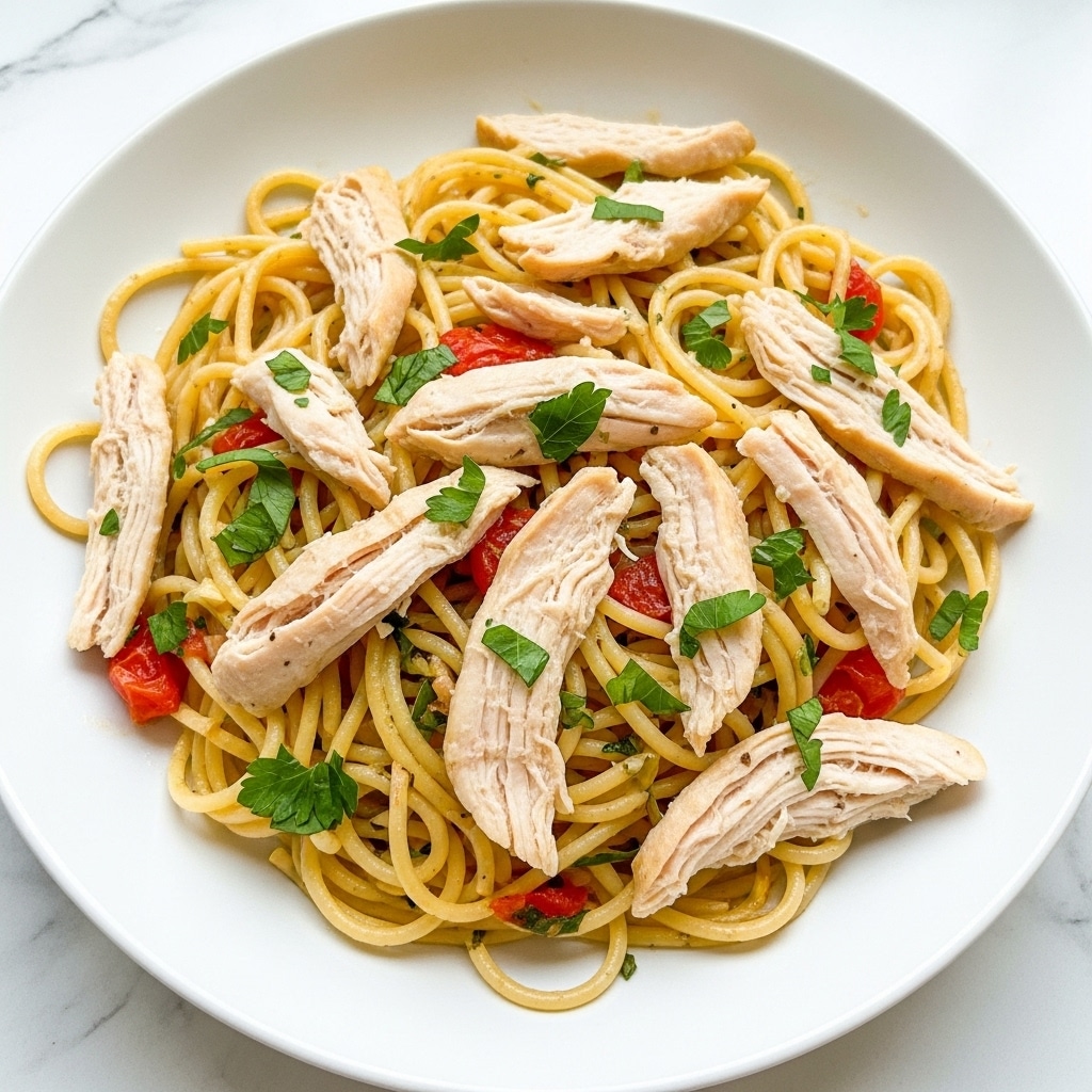 A white plate holds a dish of spaghetti mixed with shredded chicken pieces. The pasta is coated lightly with oil and has small bits of red tomato and green parsley scattered throughout. The shredded chicken is pale with a slightly browned texture, sitting evenly on top and throughout the pasta. The herbs add small pops of bright green color, while the pasta strands are golden yellow and glossy. The plate is placed on a white marbled surface. photo taken with an iphone --ar 4:5 --v 7