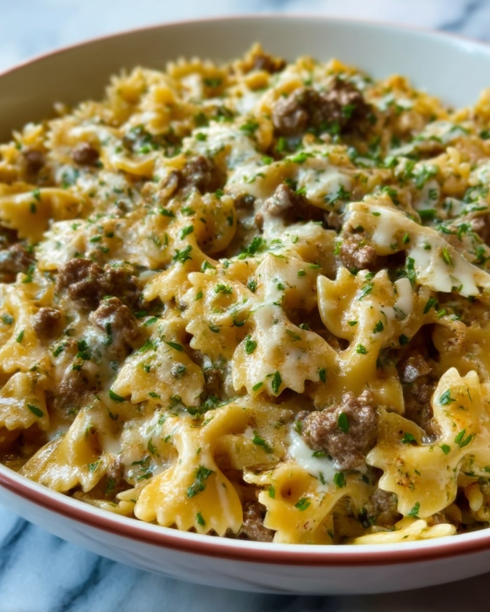 The image shows a close-up of a pasta dish with bowtie noodles mixed with small pieces of browned ground meat. It is topped with melted cheese that looks creamy and slightly bubbly, and sprinkled with chopped green herbs. The colors are warm with light yellow and brown from the pasta and meat, and bright green from the herbs. The dish is served in a white bowl placed on a white marbled surface. Photo taken with an iphone --ar 4:5 --v 7