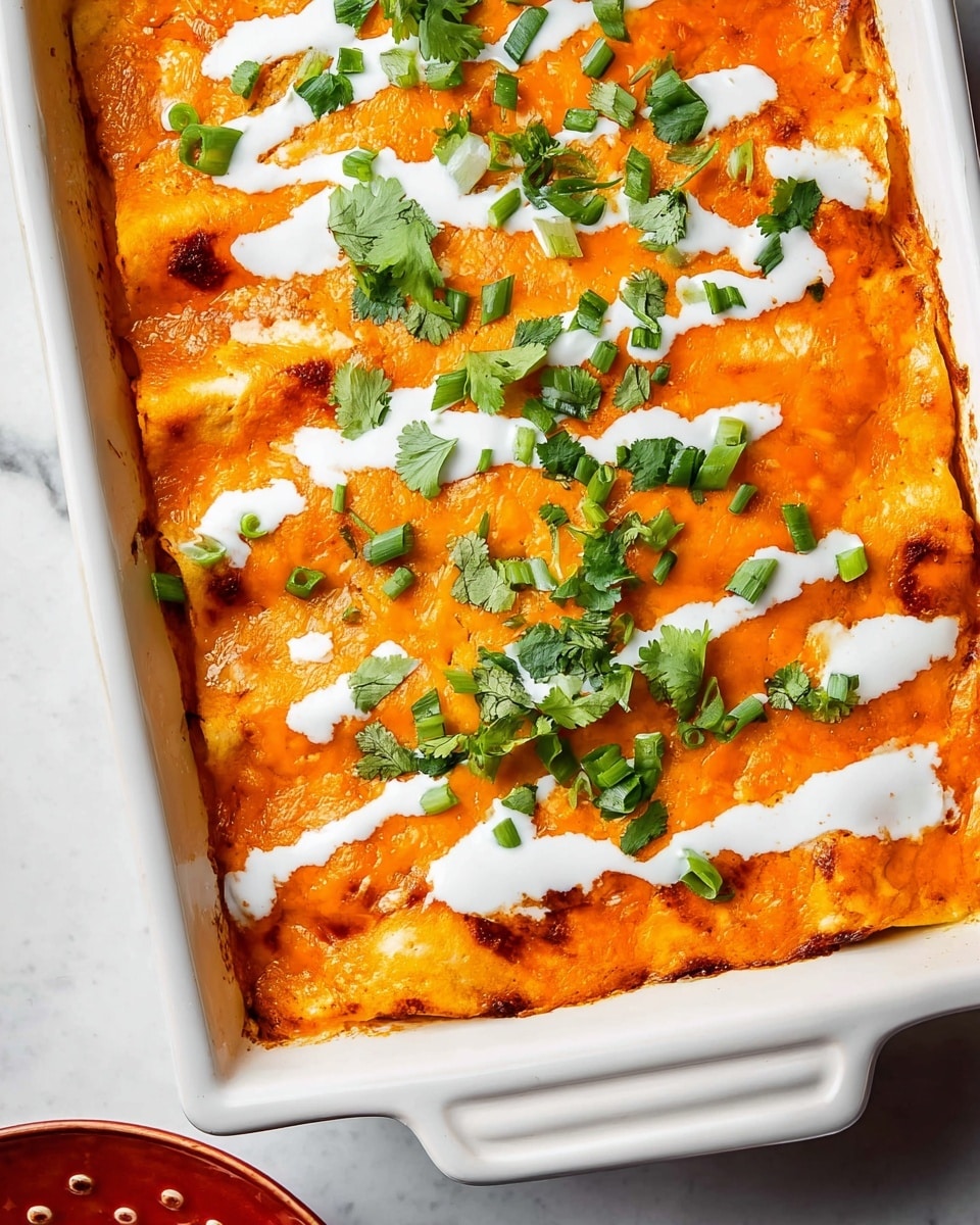 This dish is a baked casserole in a white ceramic dish. The top layer is bright orange melted cheese with some browned edges, showing a smooth and slightly bubbly texture. On top, there are creamy white sauce drizzle streaks spread unevenly across the surface. Fresh green chopped scallions and cilantro leaves are scattered on top, adding a fresh contrast to the orange and white layers. The dish sits on a white marbled surface with a small part of a red bowl visible in the corner. Photo taken with an iphone --ar 4:5 --v 7